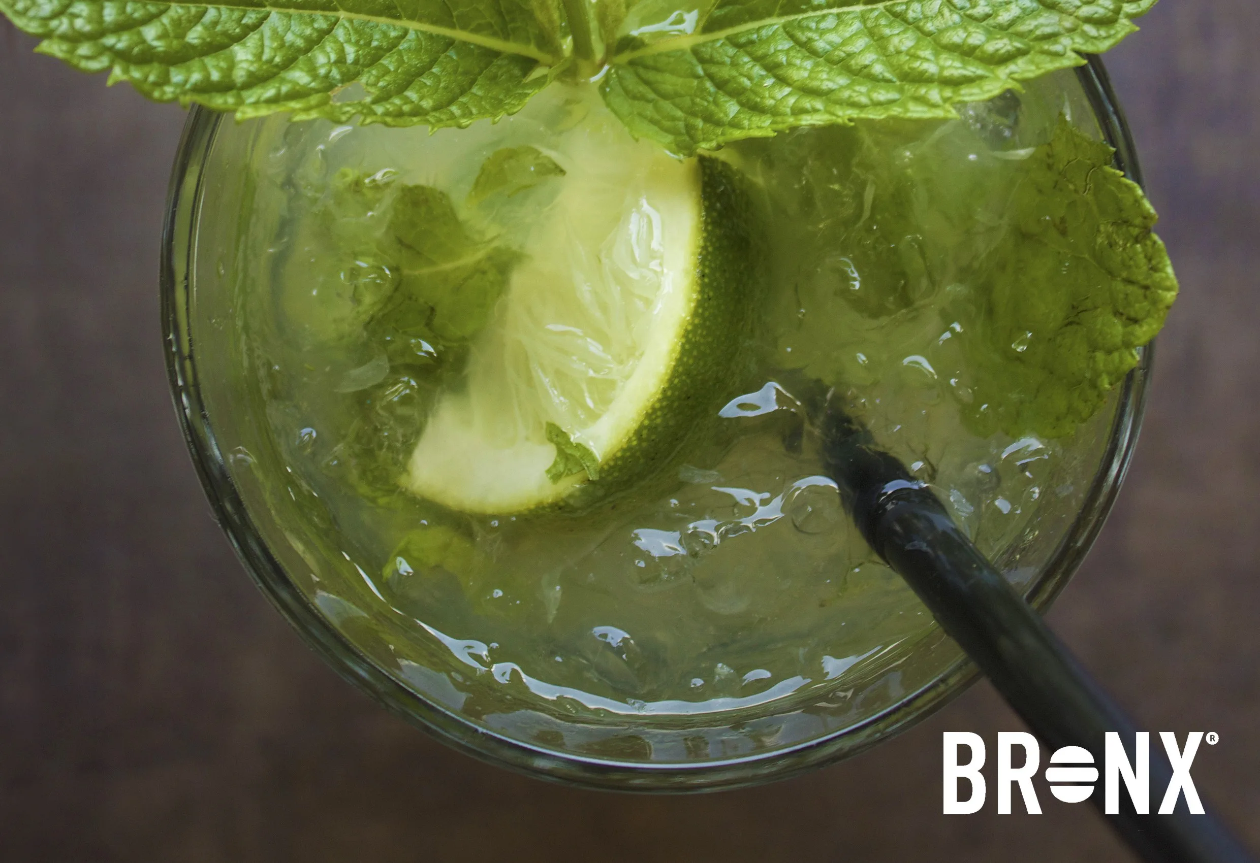 Ett grönt glas med limeklyfta och mynta sett uppifrån, med Bronx logotyp nere till höger