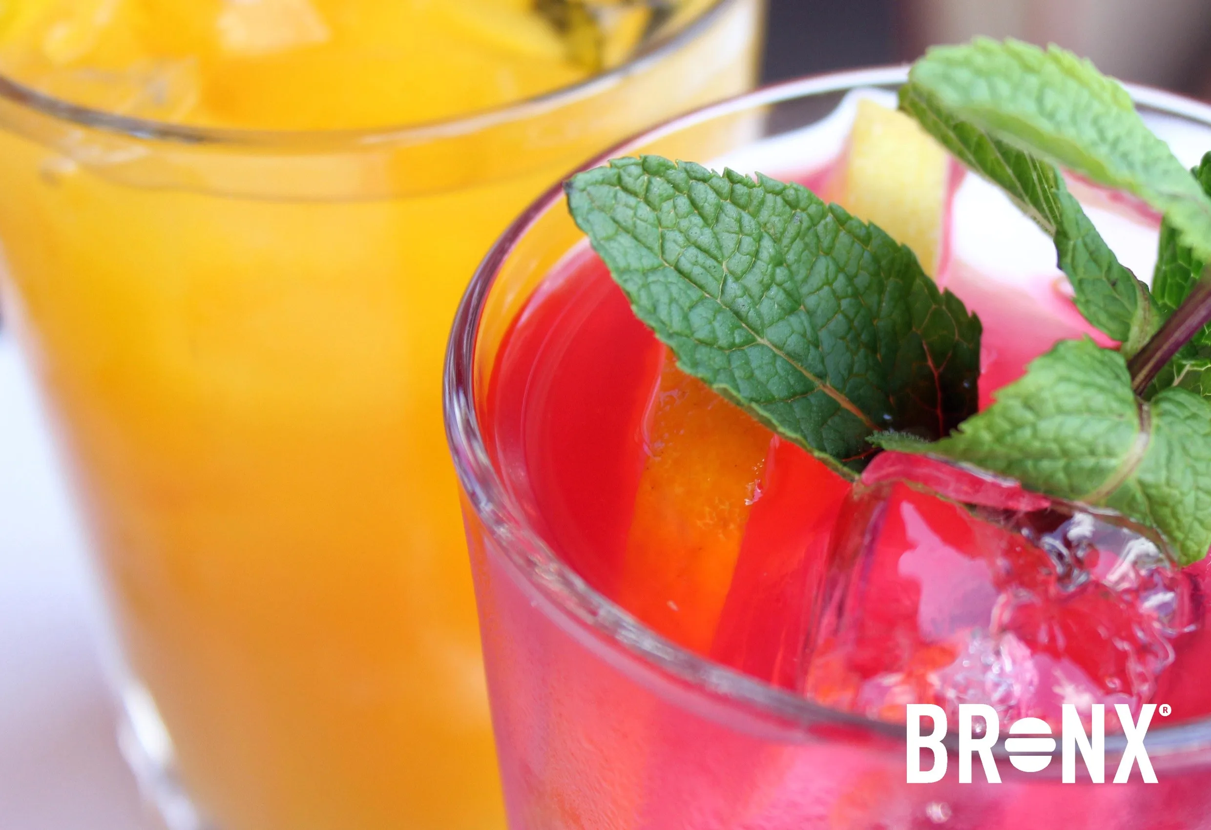 Ett glas med rosa och orange dryck och mynta, med Bronx logotyp nere till höger