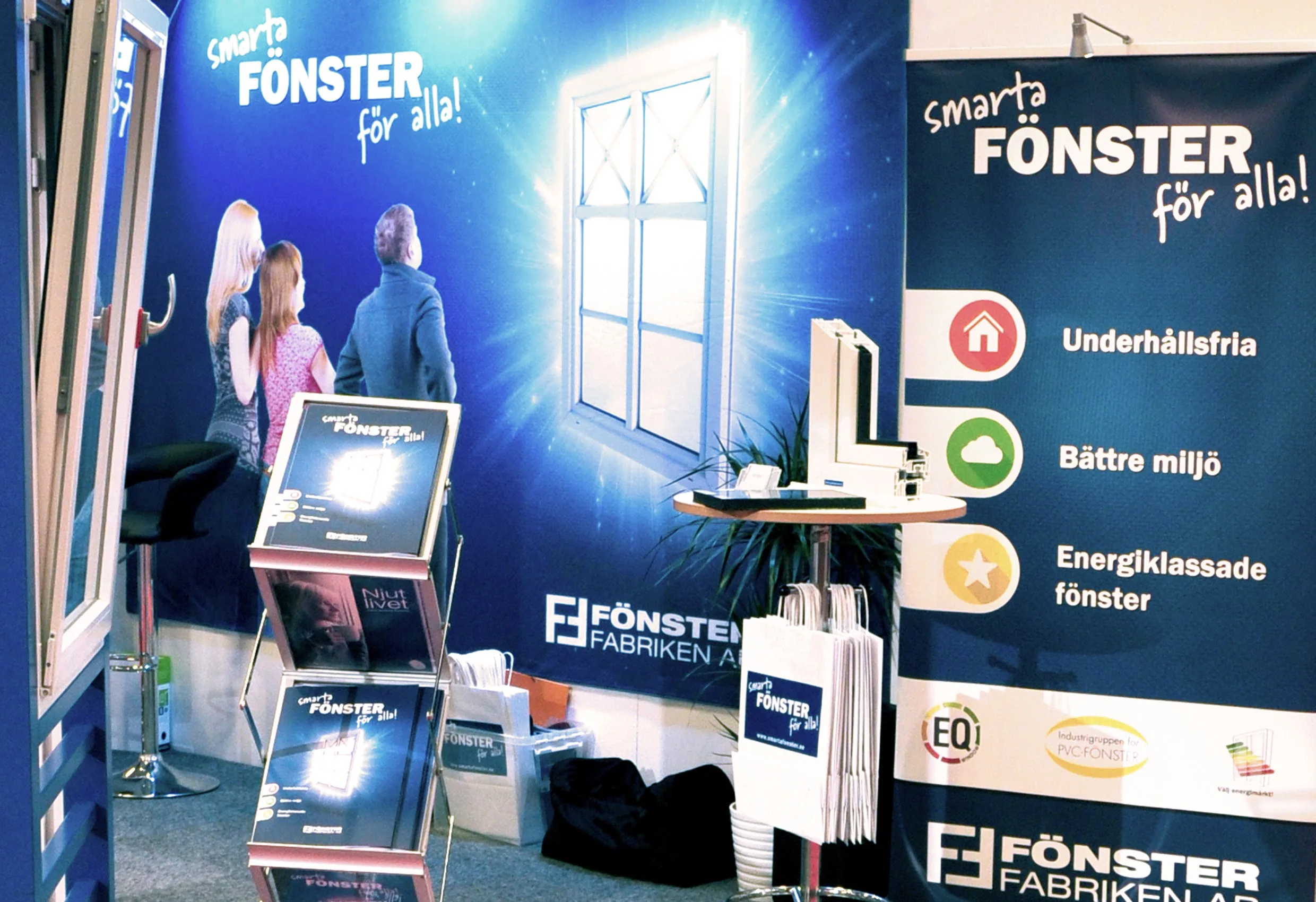 En monter med Fönsterfabrikens logotyp och texten ”Smarta fönster för alla!”, med broschyrer och en skärm