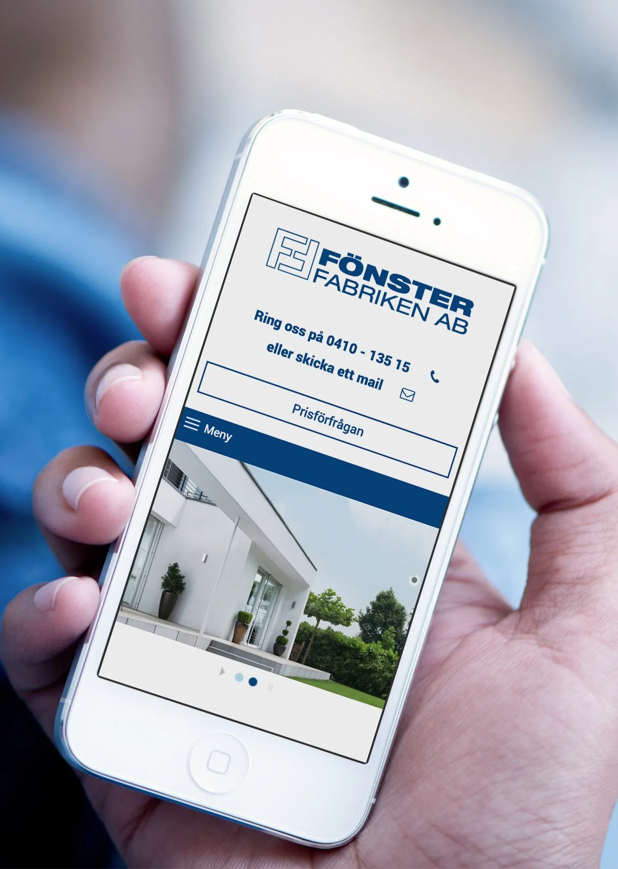 Webbplatsen på en mobil som hålls i en hand: en vit villa och rubriken med logotypen