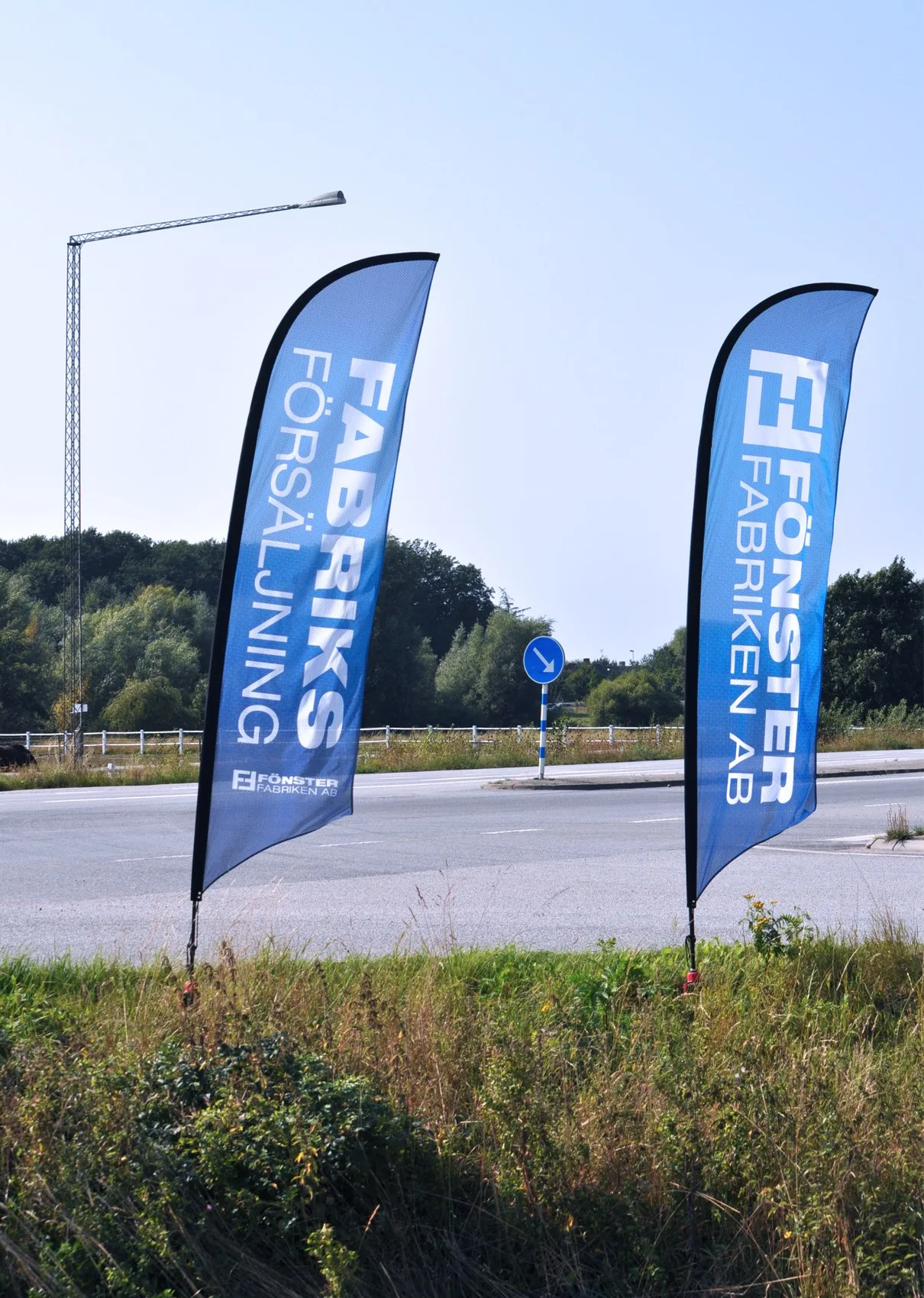 Två smala flaggor med Fönsterfabrikens logotyp vid en vägkant