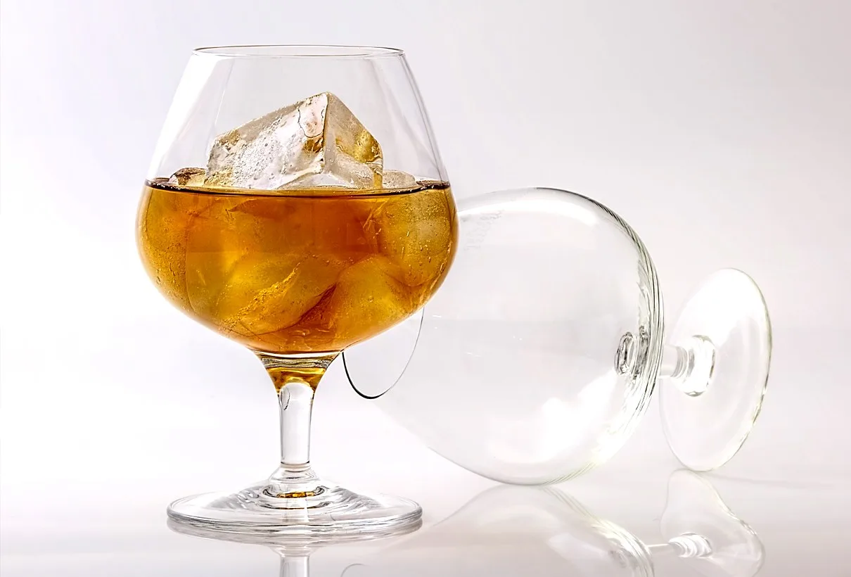 Ett konjaksglas med is och dryck, ett tippat glas bredvid