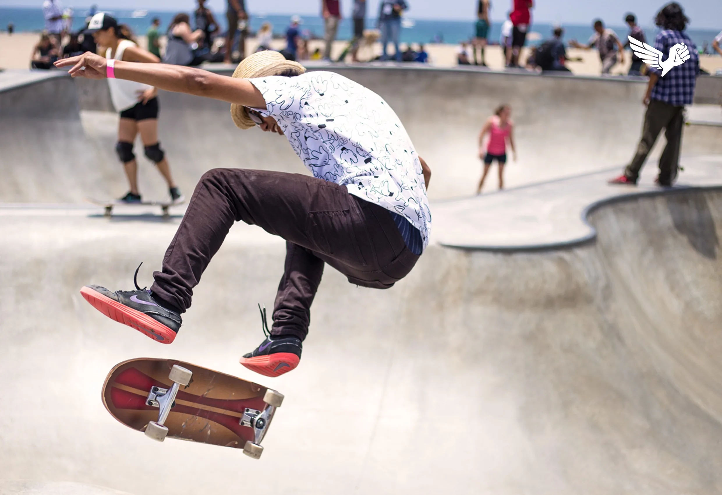 En skateboardåkare i luften i en skatepark, med en liten vingad symbol i hörnet