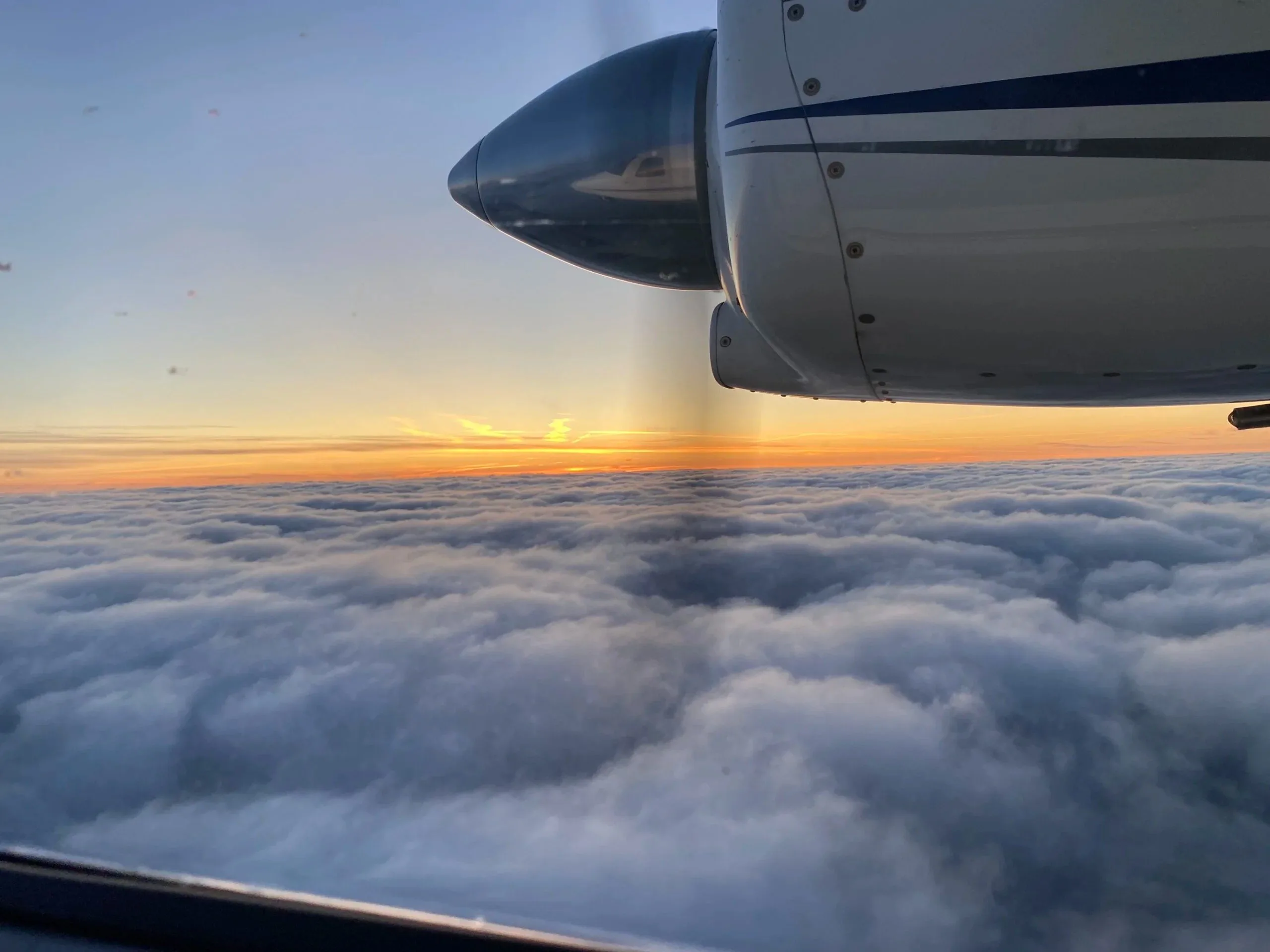 Utsikt från ett flygplan: en propeller och en vinge över ett hav av moln i solnedgång