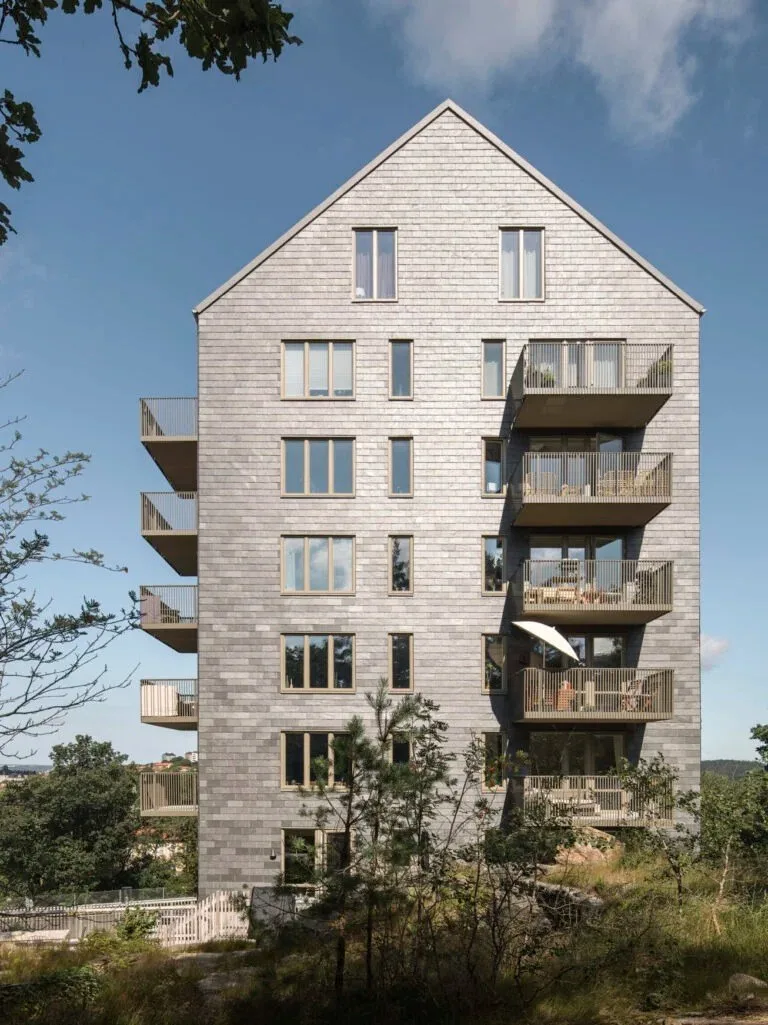 Ett flerbostadshus med balkonger och ljus tegelfasad mot blå himmel