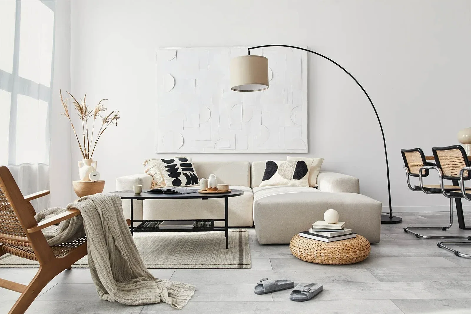 Ett ljust vardagsrum med soffa, en bågformad golvlampa, stolar och ett soffbord
