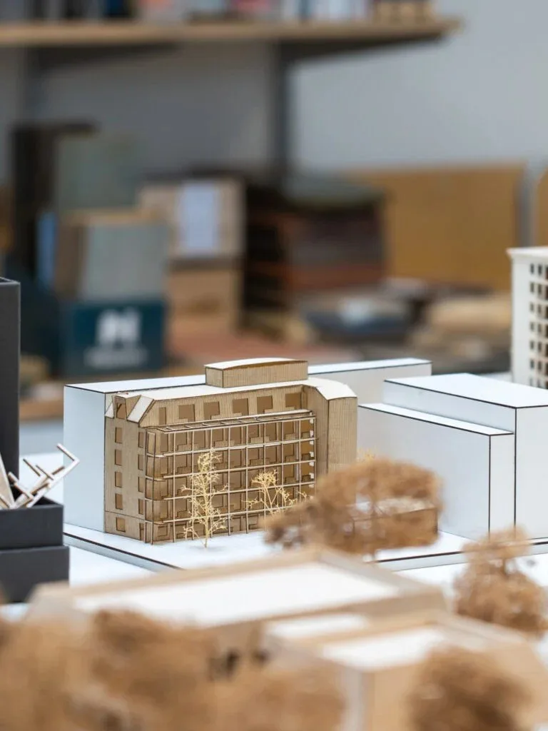 En arkitektmodell i trä framför oskarpa modeller på ett bord