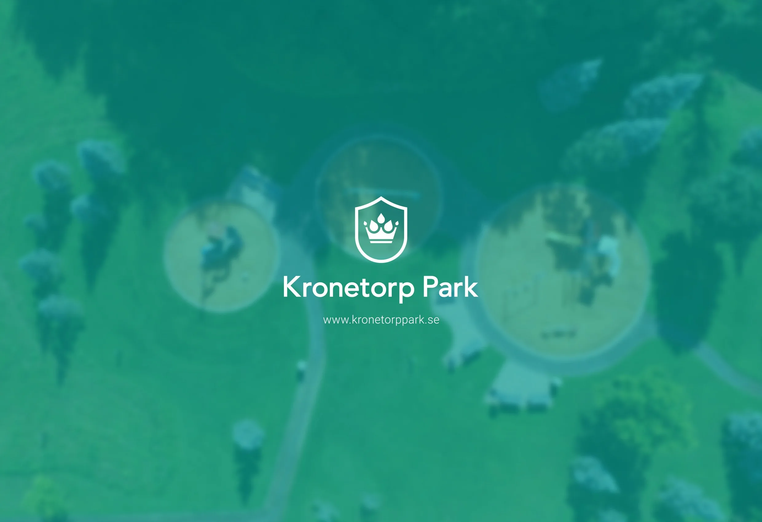 Kronetorp Parks logotyp i vitt på en grön flygbild av en park