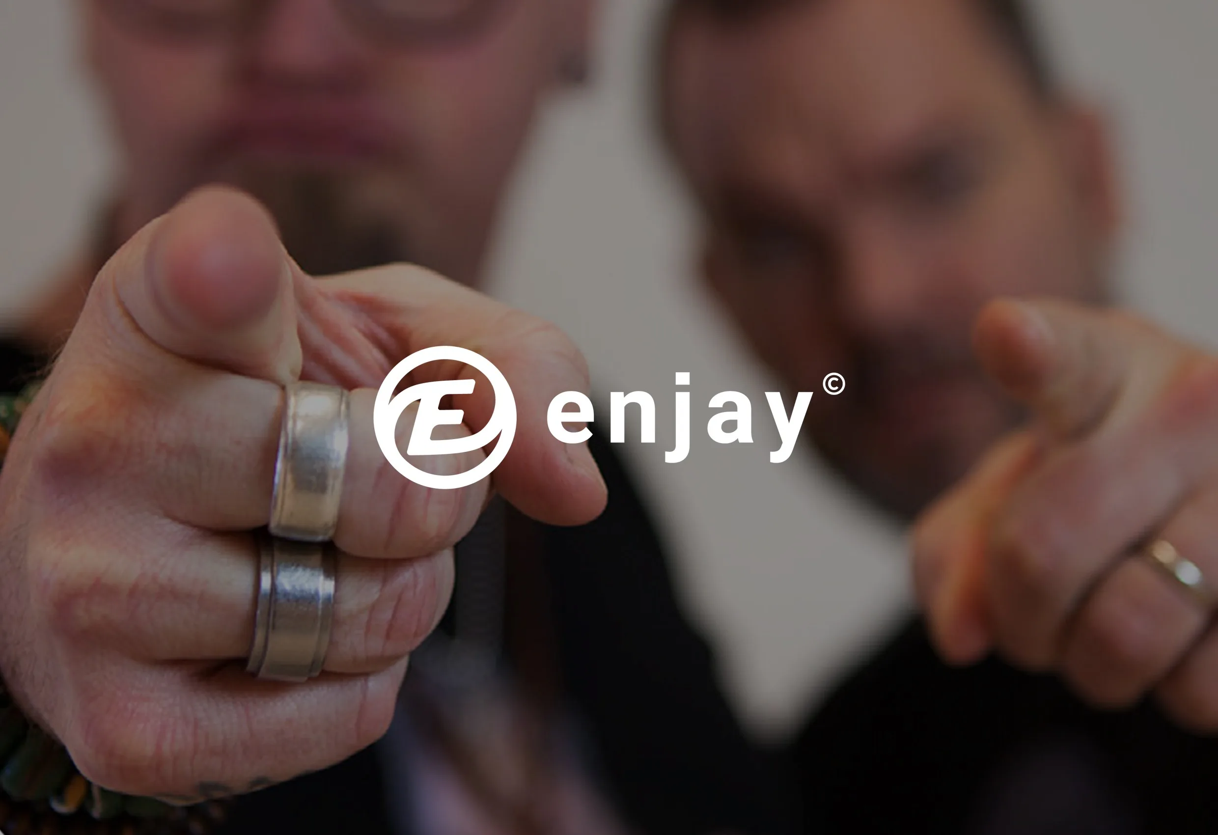 Två suddiga män bakom en hand som pekar mot kameran, med Enjays logotyp i mitten