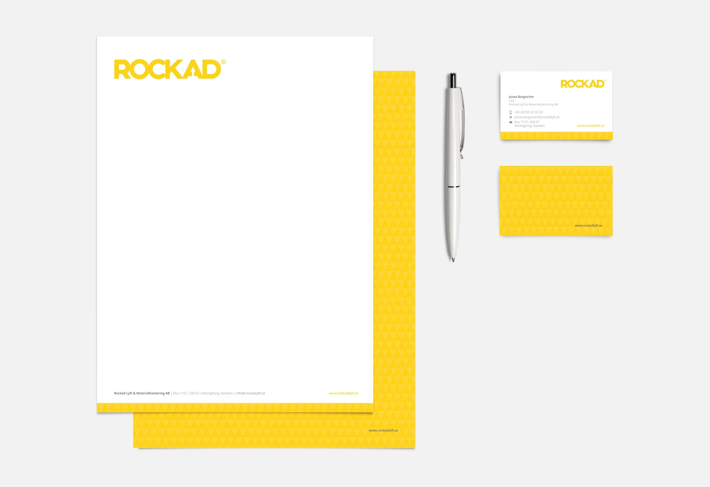 Brevpapper, kuvert, visitkort och en penna i gult och vitt med Rockads logotyp