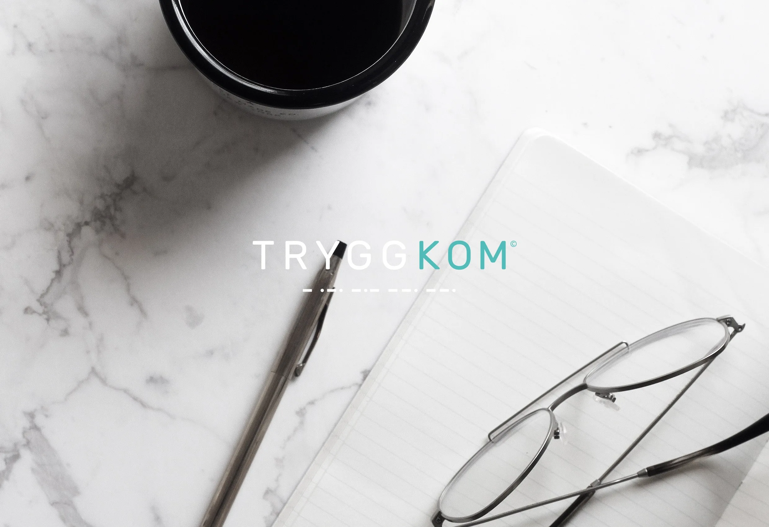 Logotypen Tryggkom i vitt och turkost ovanpå en marmorbänk med en penna, ett anteckningsblock och glasögon