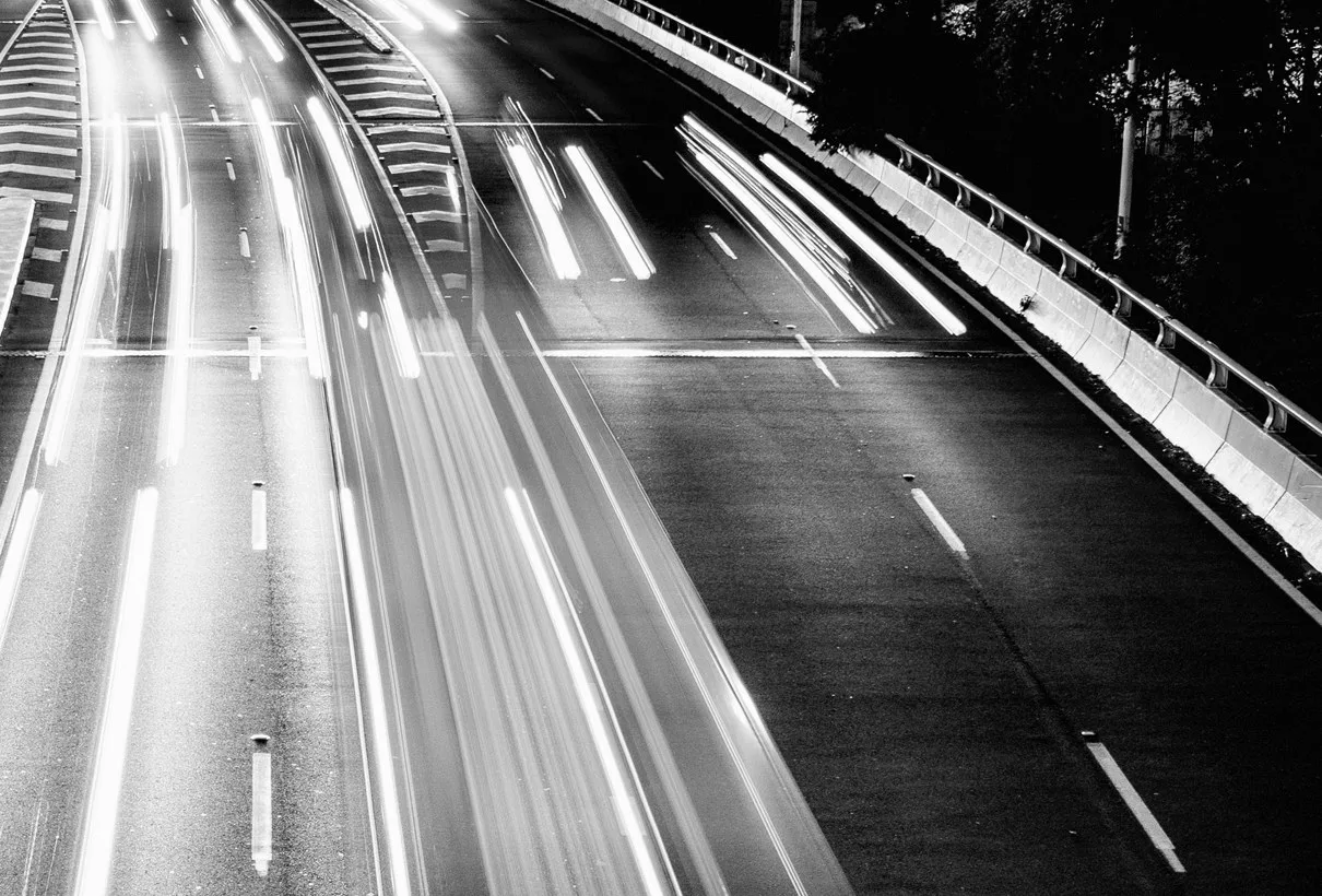 En motorväg med ljusstreck sedd uppifrån i svartvitt
