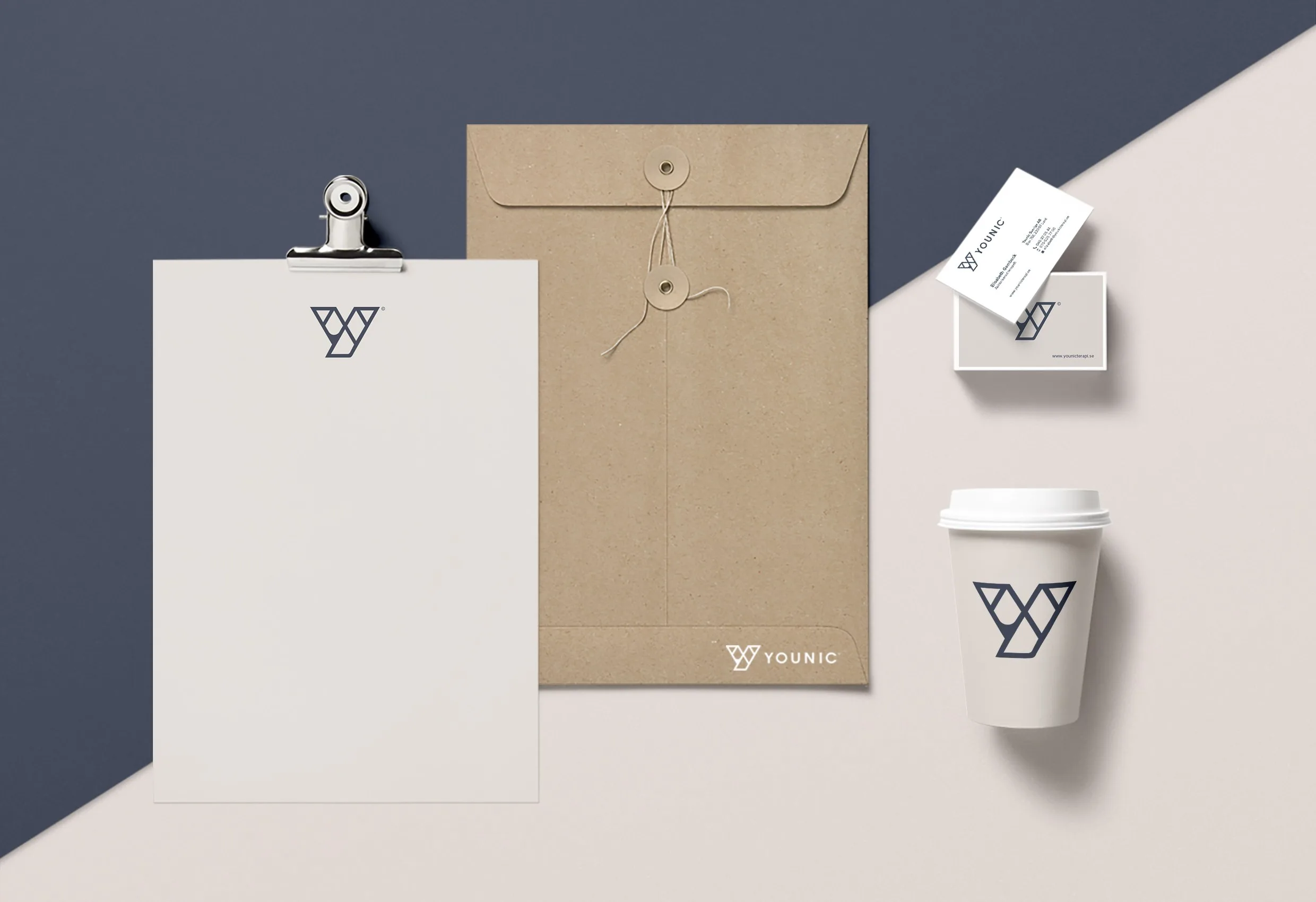 Brevpapper, kuvert, visitkort och en kaffemugg med Younics Y-symbol, på en grå och brun bakgrund